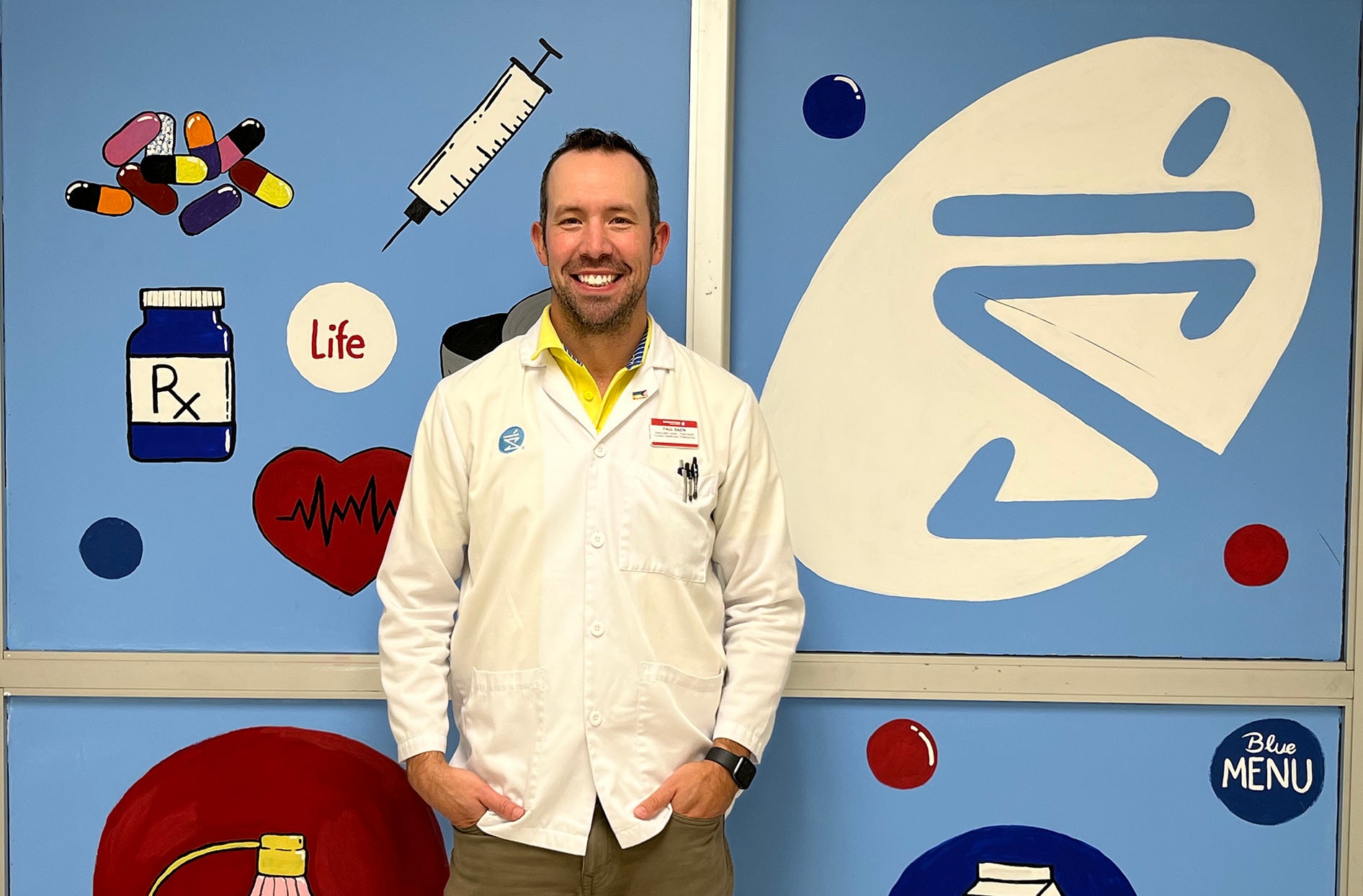 Paul stands inside his store smiling in front of a colourful wall. 