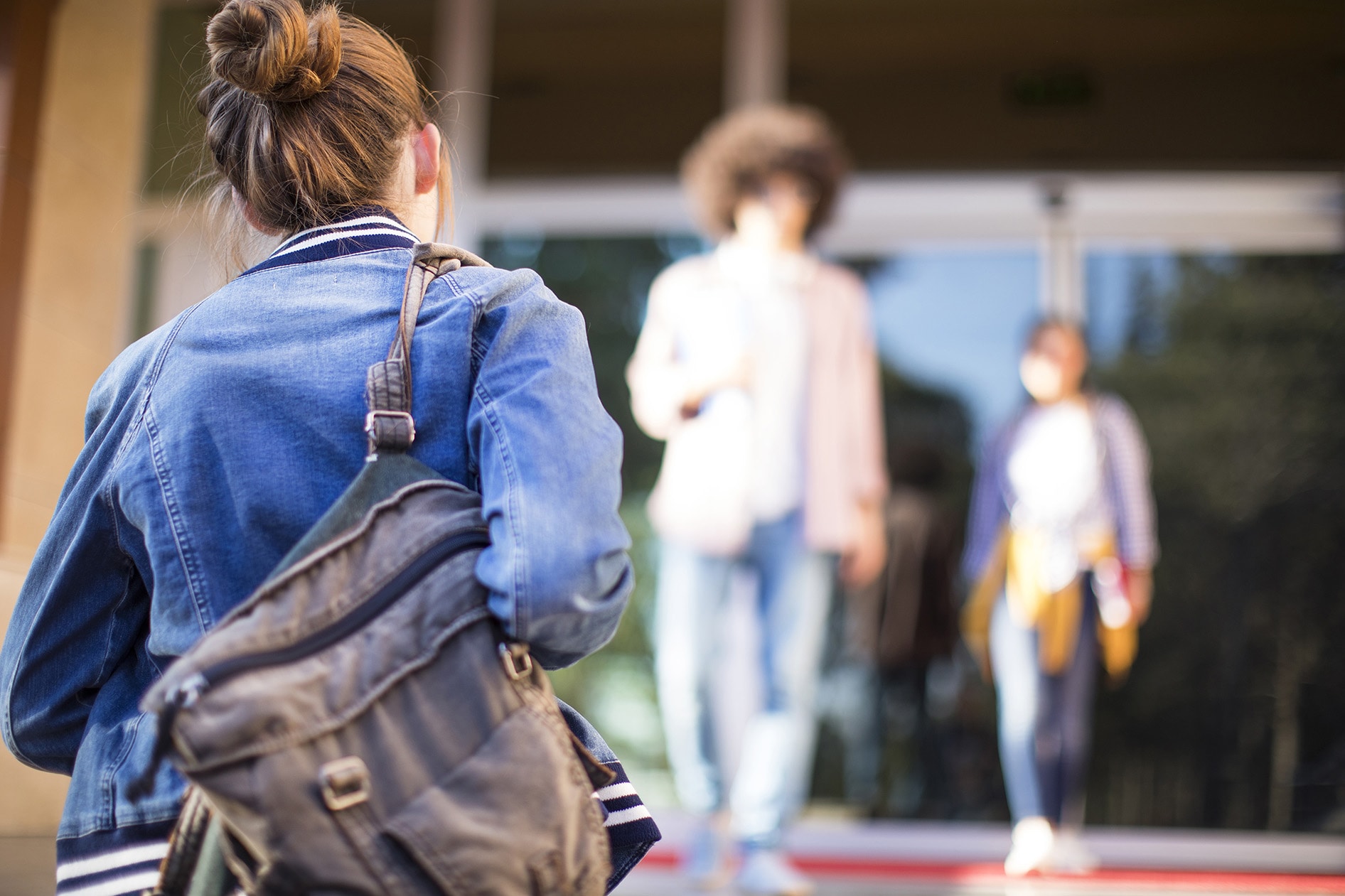 The back of a young girl walking forward carrying a school bag