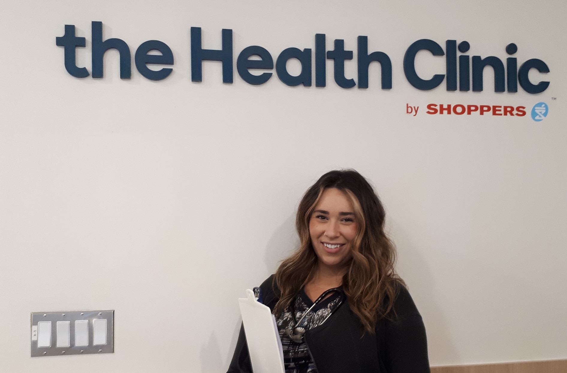 Rebekah stands in front of a “The Health Clinic by Shoppers” sign. 