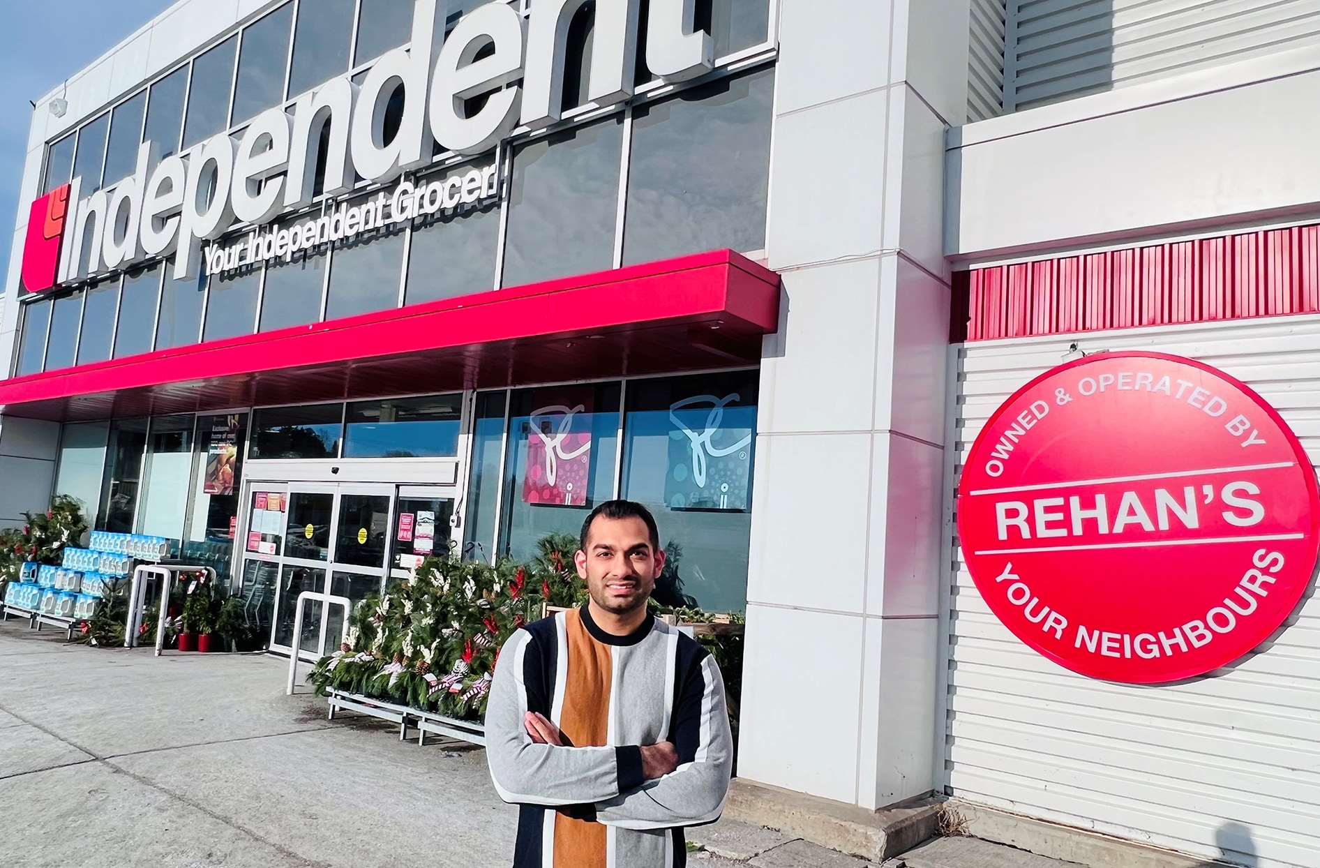 Rehan stands outside with his store and the Your Independent Grocer sign in the background.
