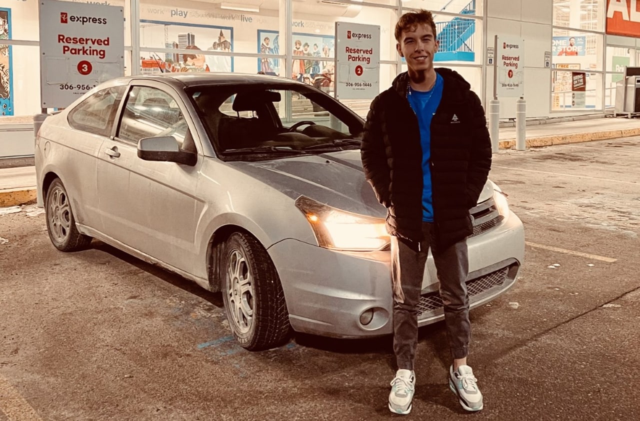 Teenage boy standing next to car in store parking lot