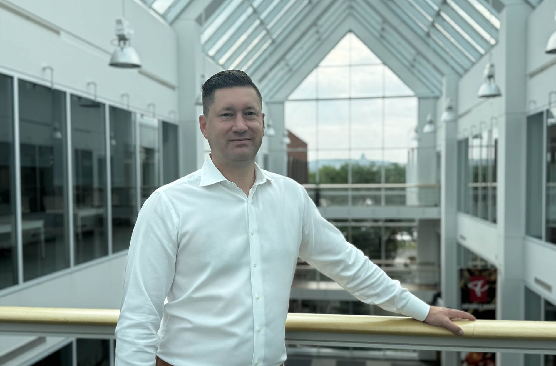 A photo of Sylvain leaning against a railing with his left arm stretched out, smiling.
