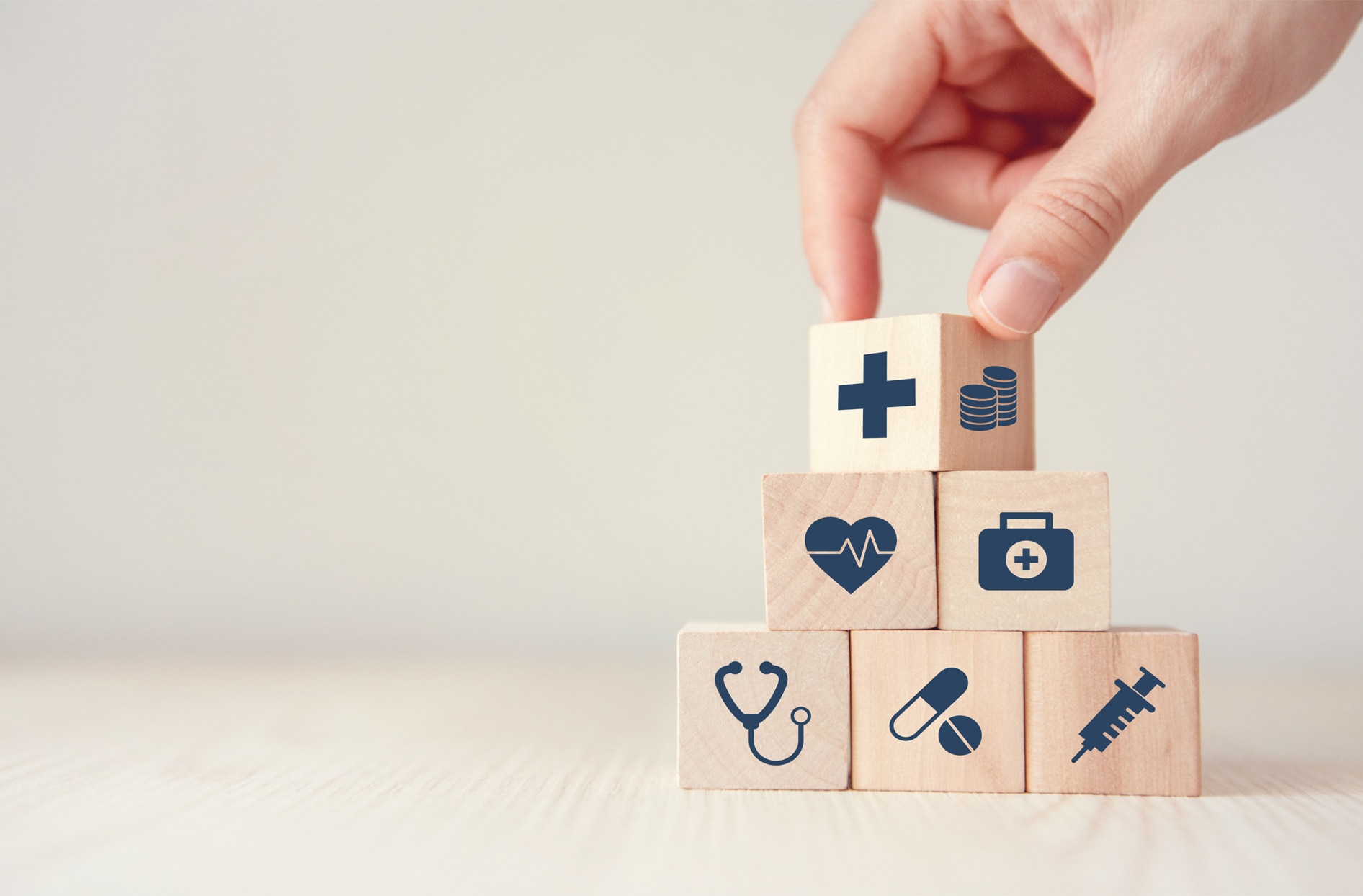 A hand stacking mini wooden cubes with healthcare symbols on them. 