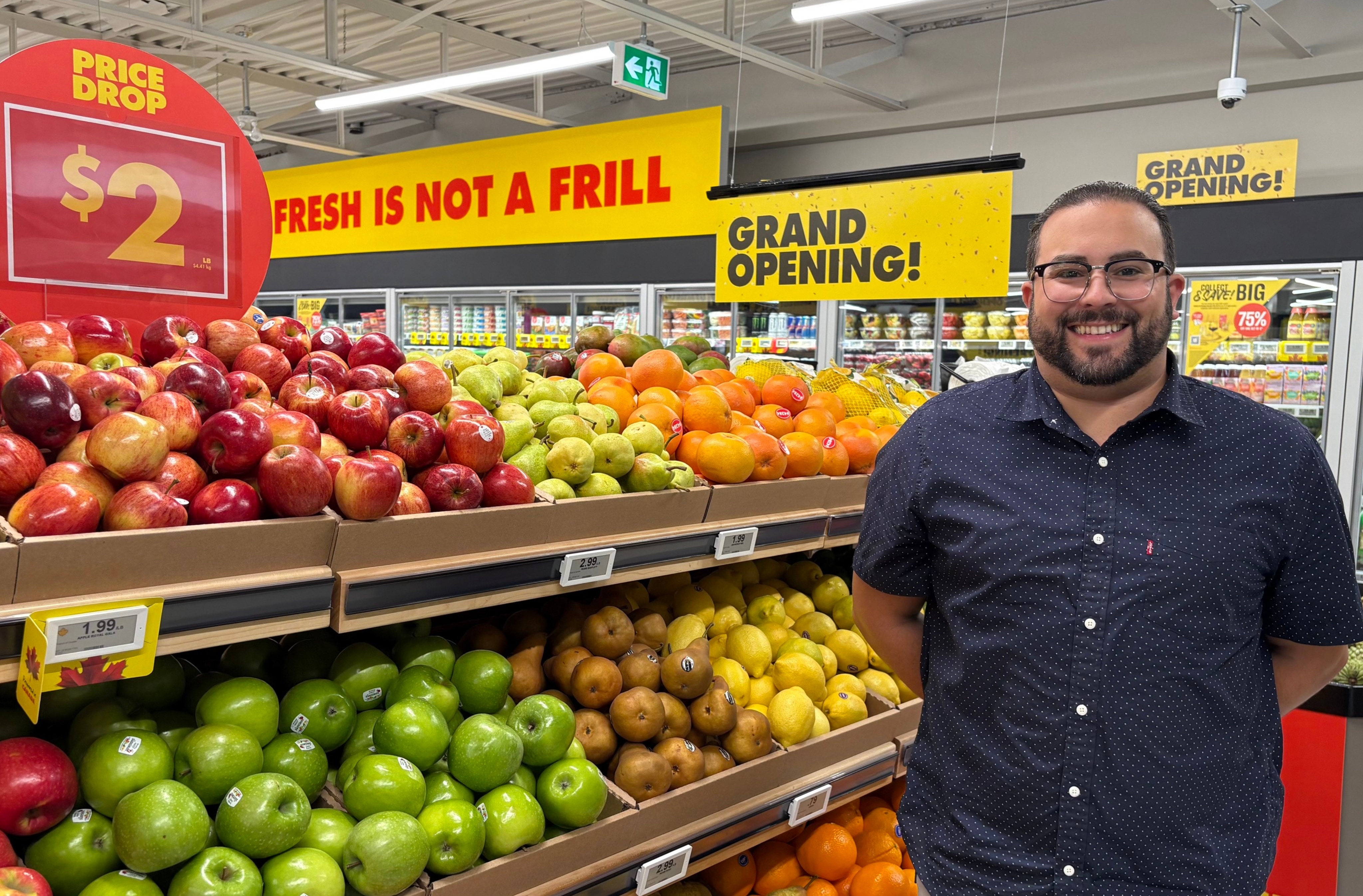 Tyler Amaral smiling in front of a colorful fruit display at a No Frills store
