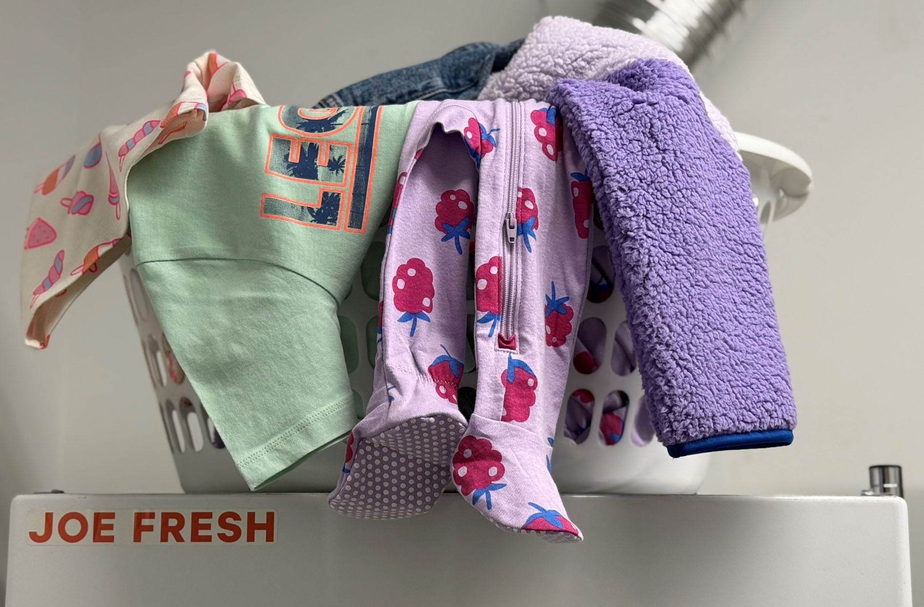 Laundry basket full of Joe Fresh clothes on top of a washing machine.