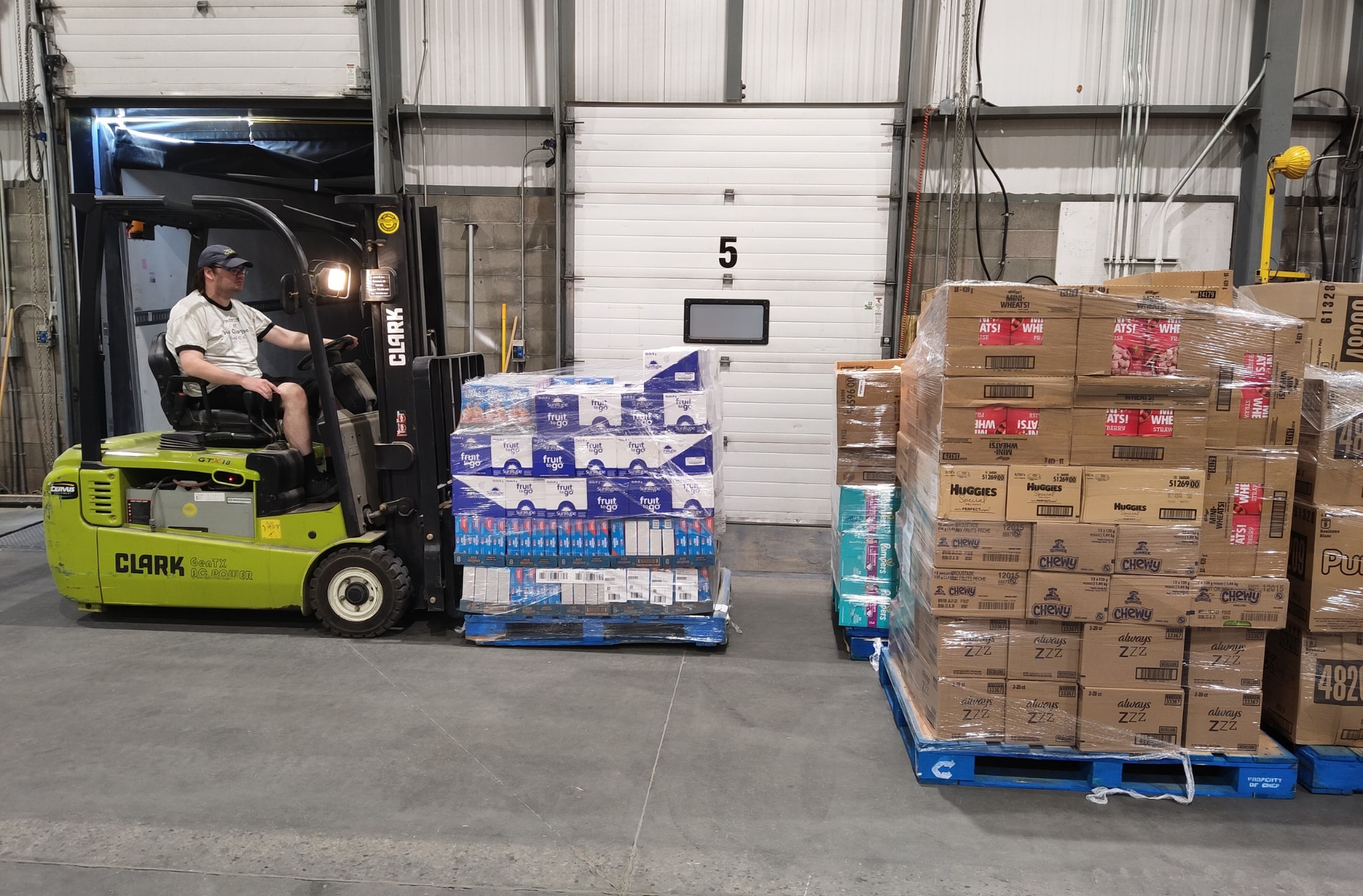 A colleague uses a lift truck to move a pallet of different food items. 