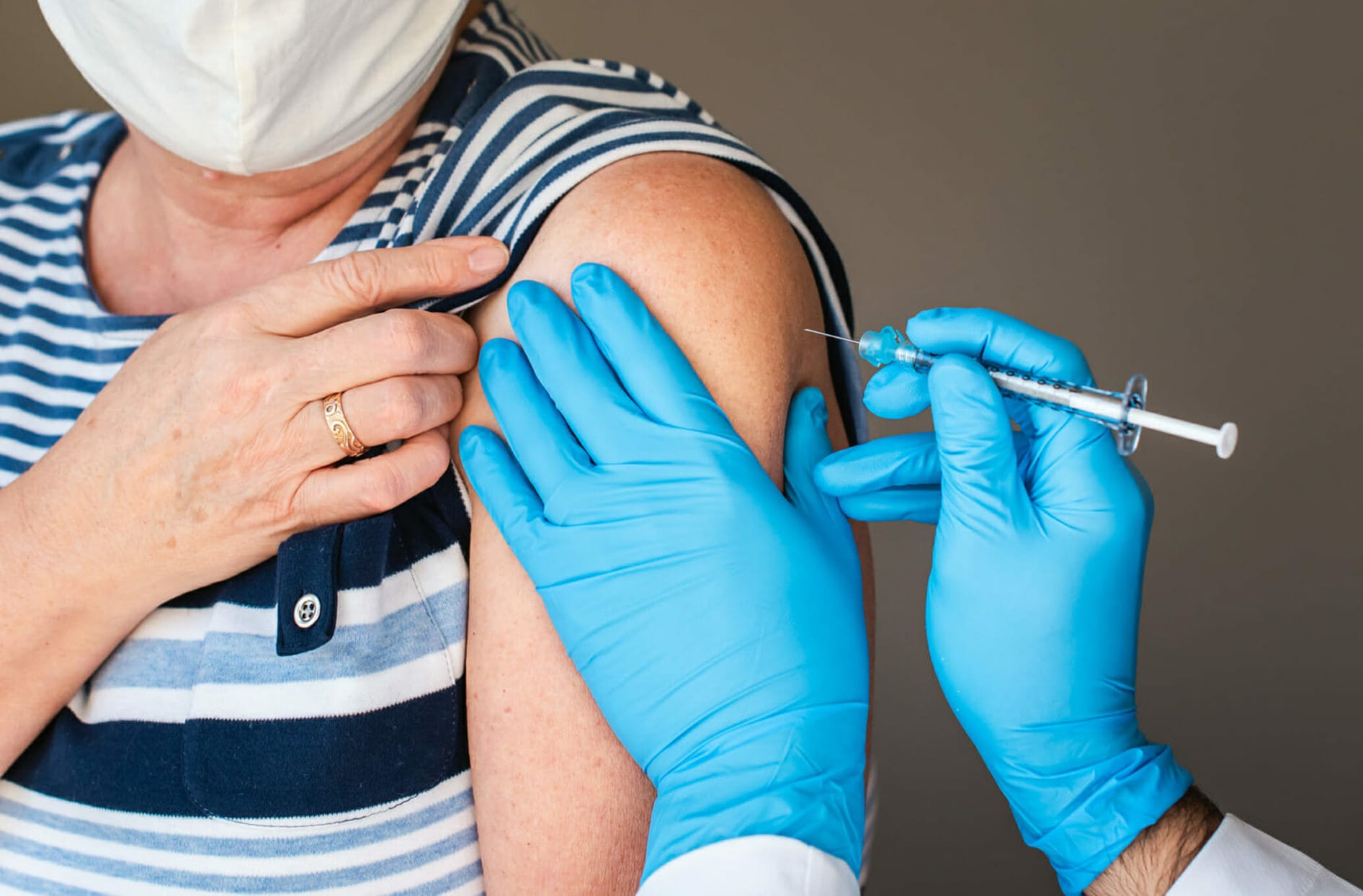 An unidentifiable woman wearing a face mask gets a shot in her left arm 