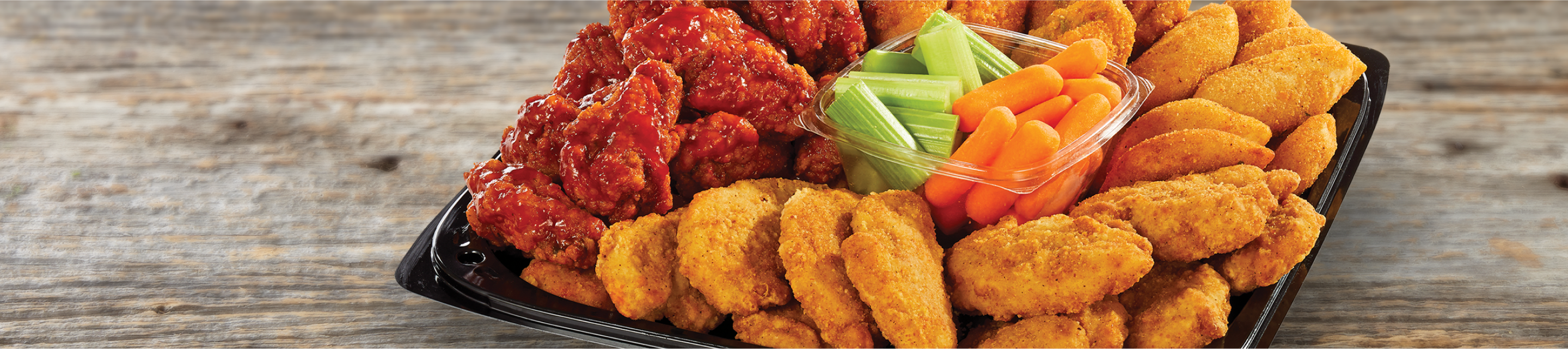 Tray of assorted chicken wings and nuggets with vegetables in the middle