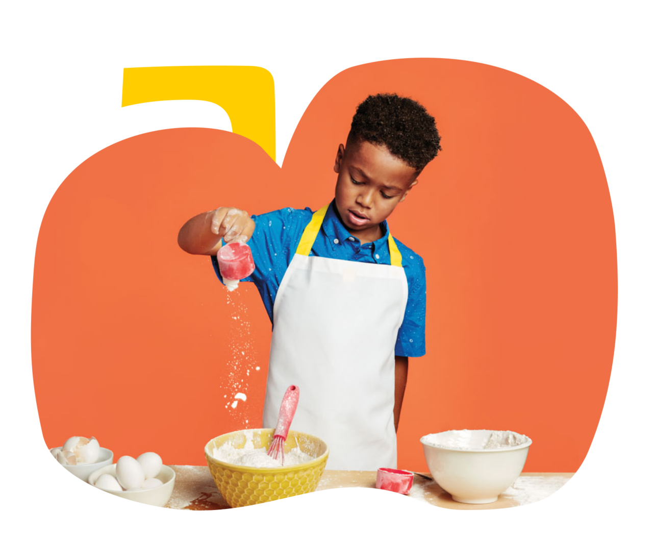 Young boy pouring a cup of flour into a mixing bowl.