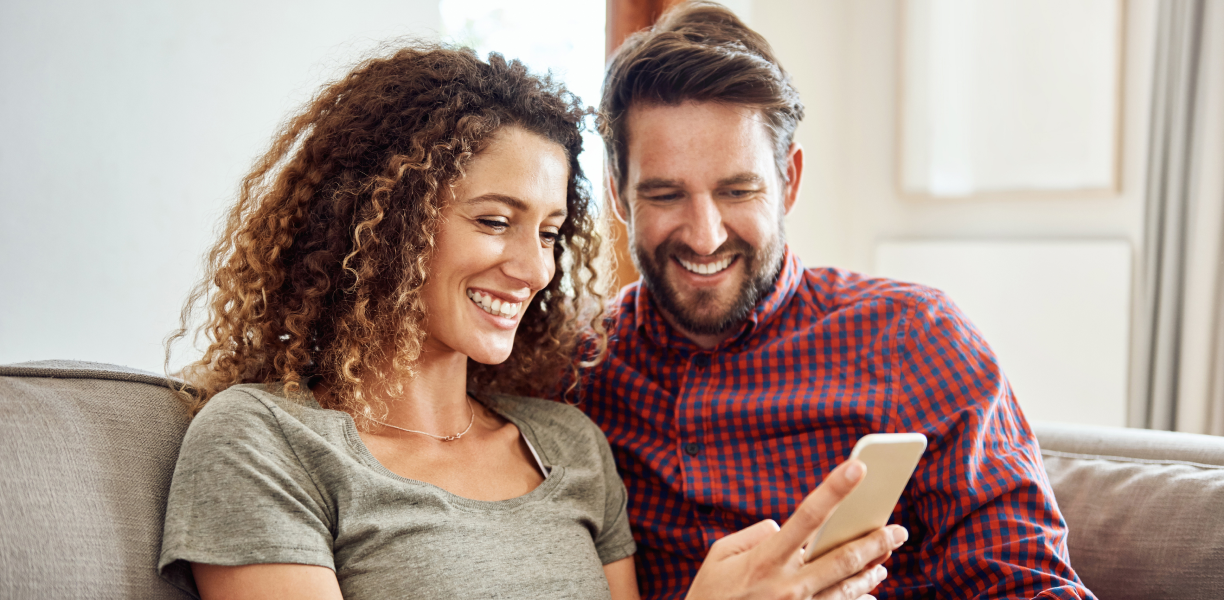 Two friends at home smiling at a phone. A young family in joyous embrace. 