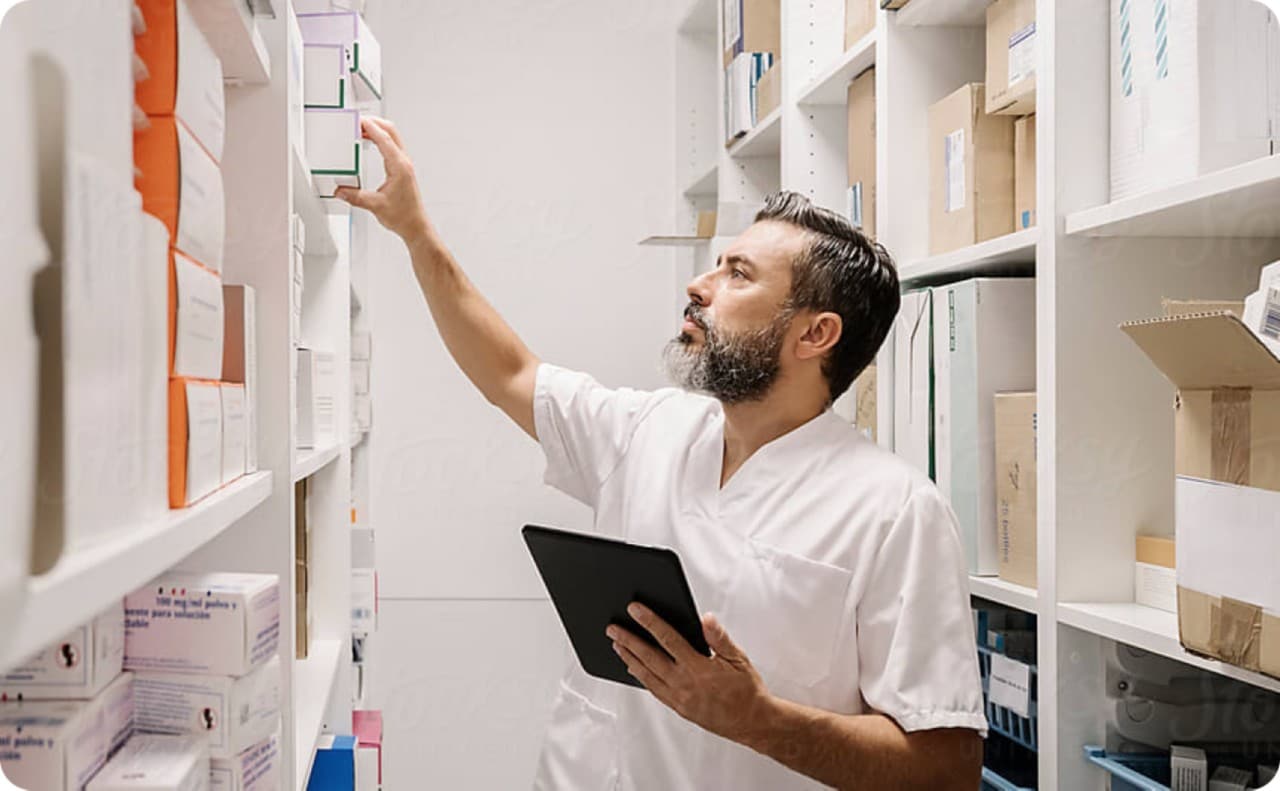 Man in white coat reaching for boxes in stock room.