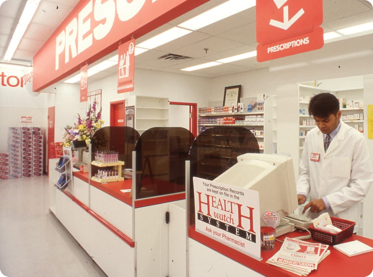 Intérieur d’une pharmacie Shoppers Drug Mart avec une personne portant une blouse blanche pour travailler.