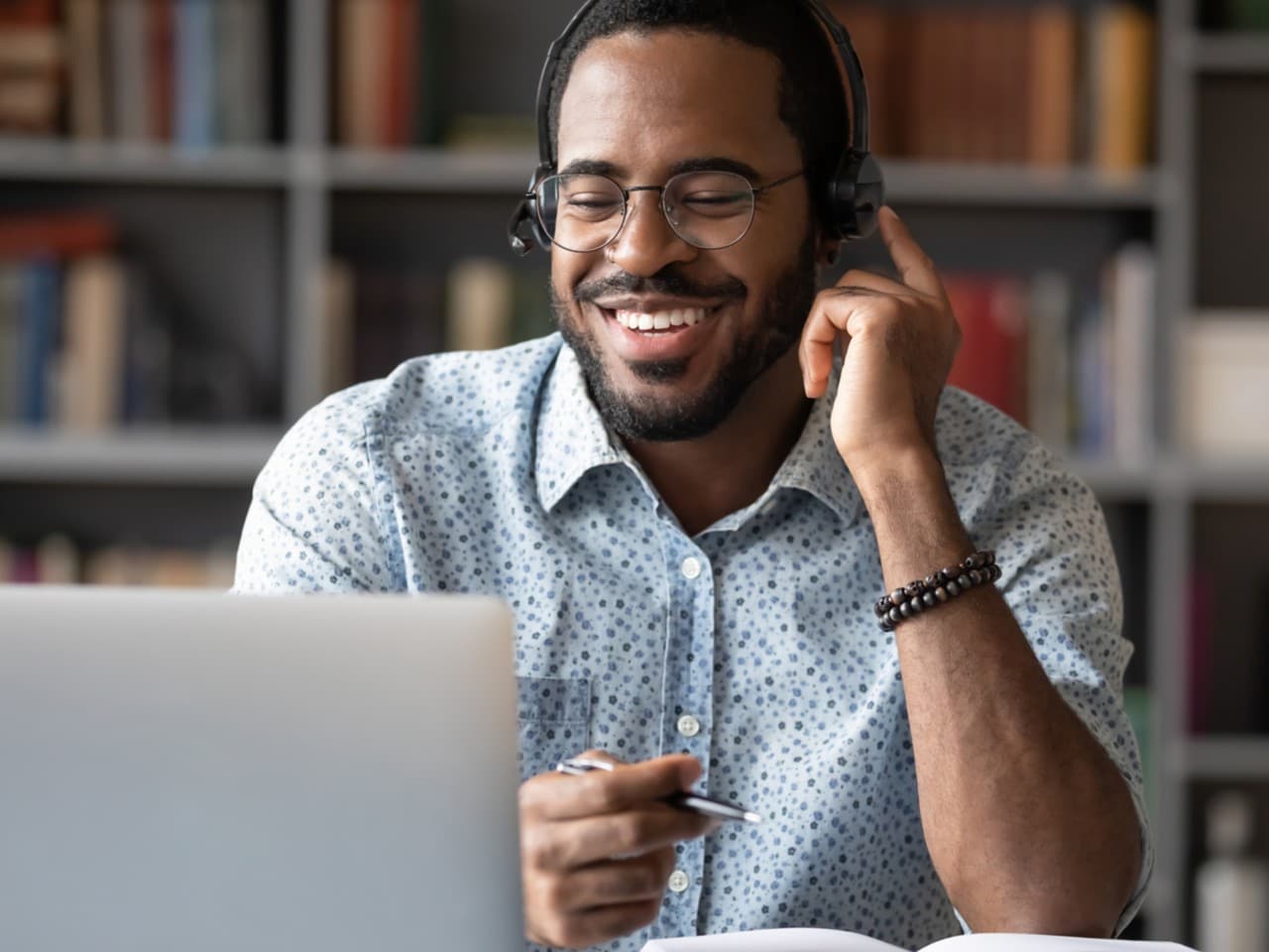 Homme souriant portant des lunettes et un casque d'écoute assis derrière un bureau